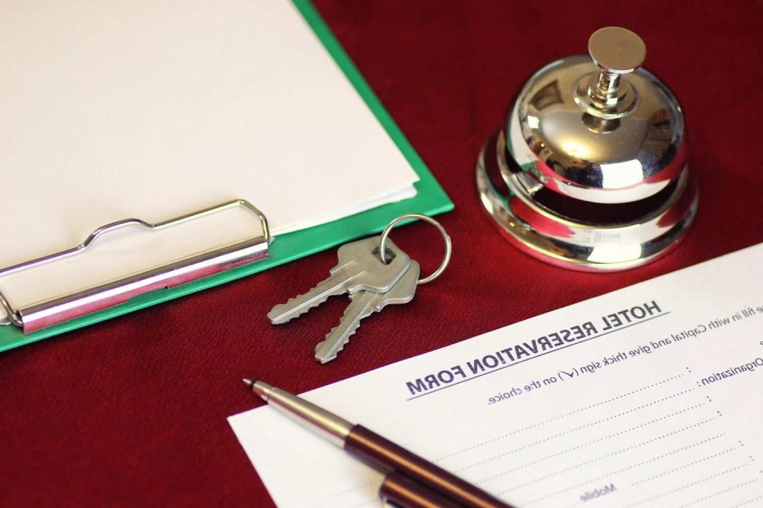Hotel reservation form on a clipboard next to room keys and a bell, showing traditional paper based check-in