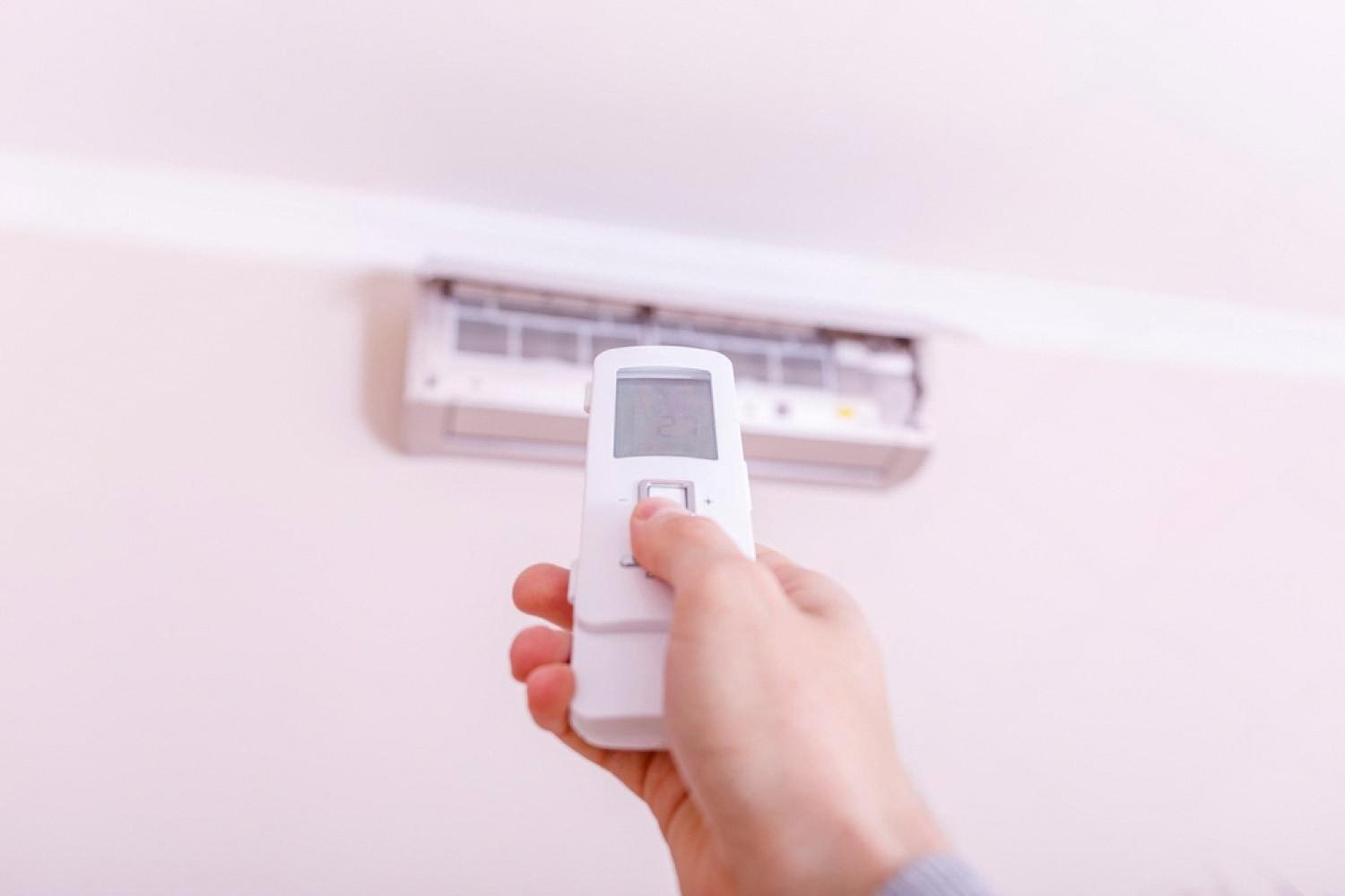 Hand pointing a remote at a wall-mounted air conditioner in a Dubai apartment